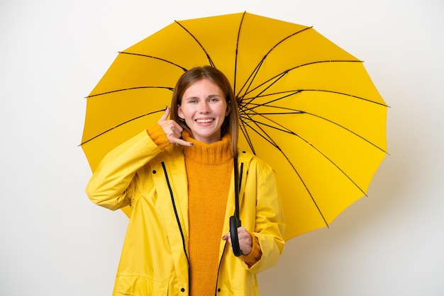 Giovane donna inglese con cappotto antipioggia e ombrello isolato su sfondo bianco che fa il gesto del telefono Call me back sign