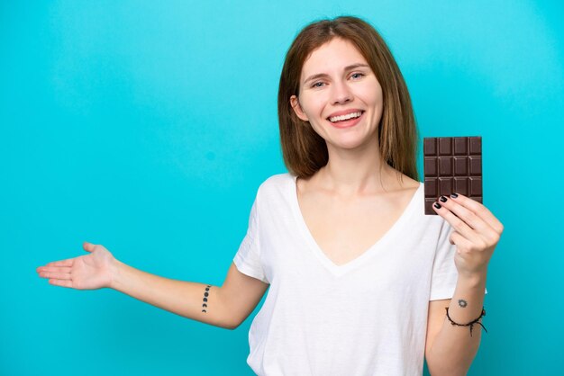 Giovane donna inglese con cioccolato isolato su sfondo blu che estende le mani di lato per invitare a venire