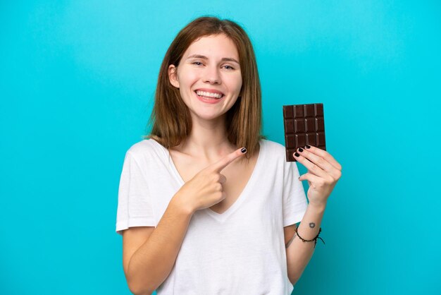 Giovane donna inglese con cioccolato isolato su sfondo blu che punta di lato per presentare un prodotto