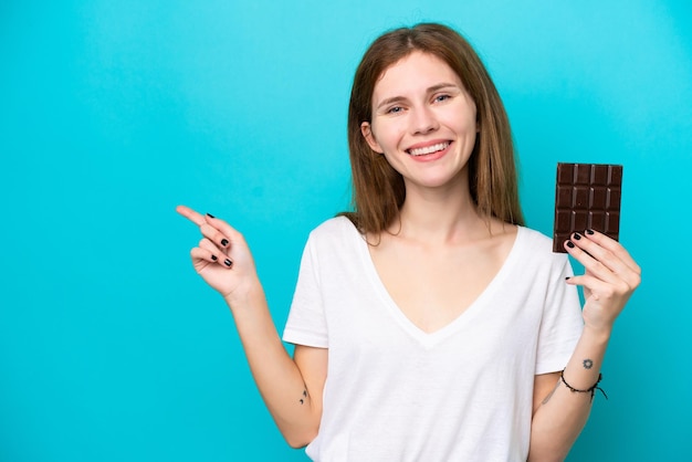 Giovane donna inglese con cioccolato isolato su sfondo blu che punta il dito di lato