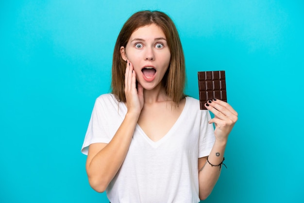 Giovane donna inglese con cioccolato isolato su sfondo blu con espressione facciale sorpresa e scioccata