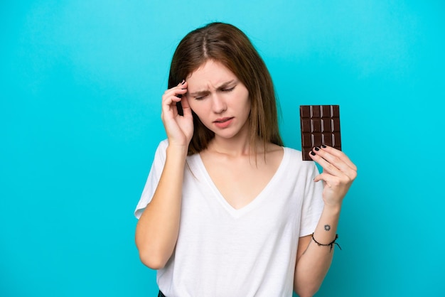 Giovane donna inglese con cioccolato isolato su sfondo blu con mal di testa