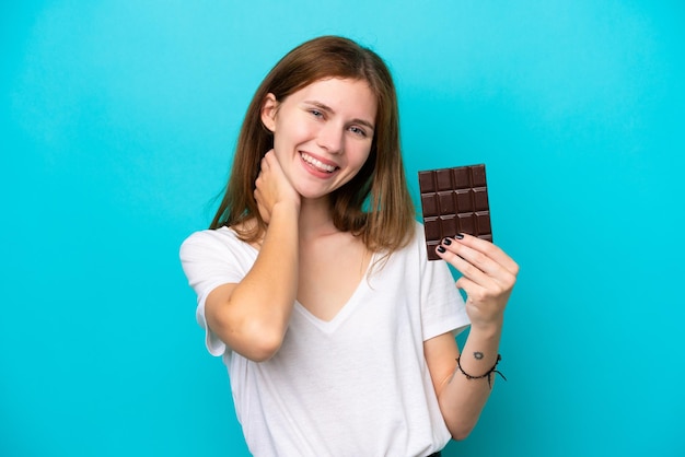 Giovane donna inglese con cioccolato isolato su sfondo blu ridendo