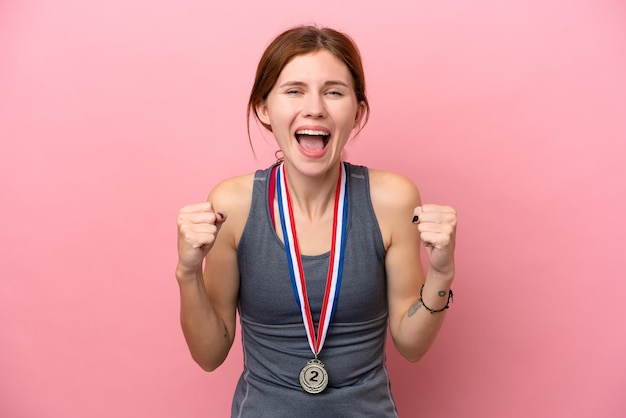 Giovane donna inglese con medaglie isolate su sfondo rosa che celebra una vittoria in posizione di vincitore