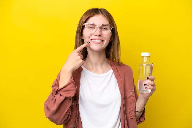 Giovane donna inglese con una bottiglia d'acqua isolata su sfondo giallo che dà un pollice in alto gesto