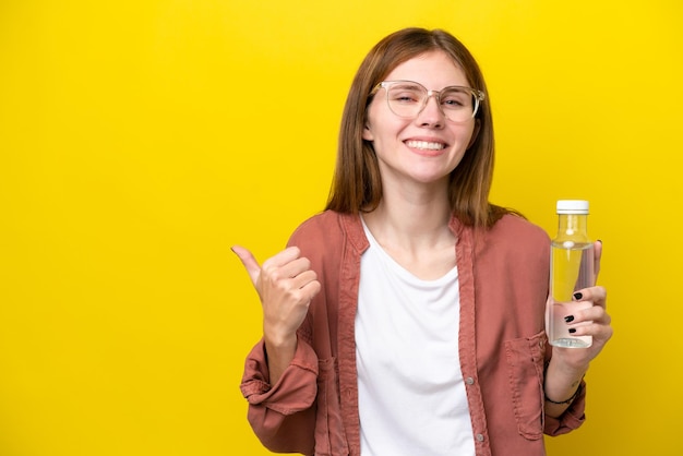 Giovane donna inglese con una bottiglia d'acqua isolata su sfondo giallo che punta di lato per presentare un prodotto