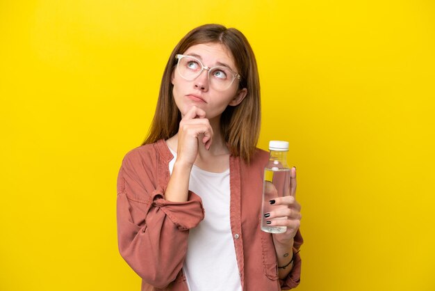 Giovane donna inglese con una bottiglia d'acqua isolata su sfondo giallo e alzando lo sguardo