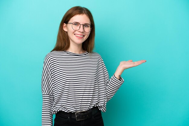 Giovane donna inglese isolata su sfondo blu che tiene copyspace immaginario sul palmo per inserire un annuncio