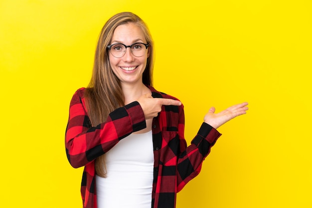 Giovane donna inglese isolata su sfondo giallo con copyspace immaginario sul palmo per inserire un annuncio