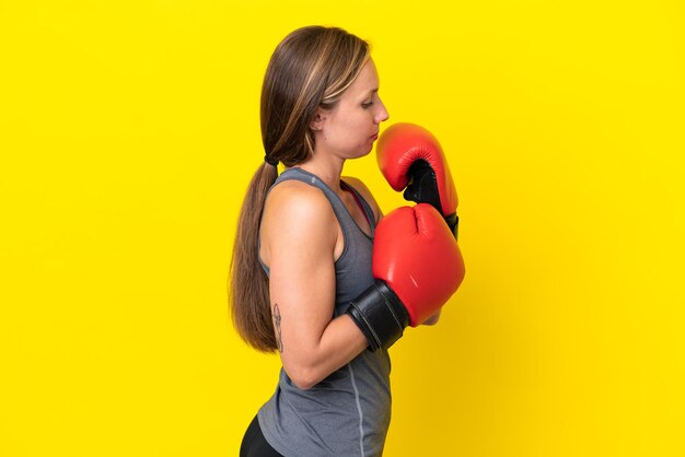 Giovane donna inglese isolata su sfondo giallo con guantoni da boxe