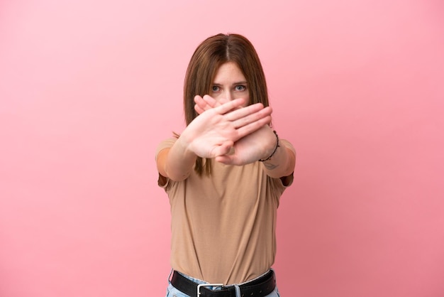 Giovane donna inglese isolata su sfondo rosa che fa un gesto di arresto con la mano per fermare un atto