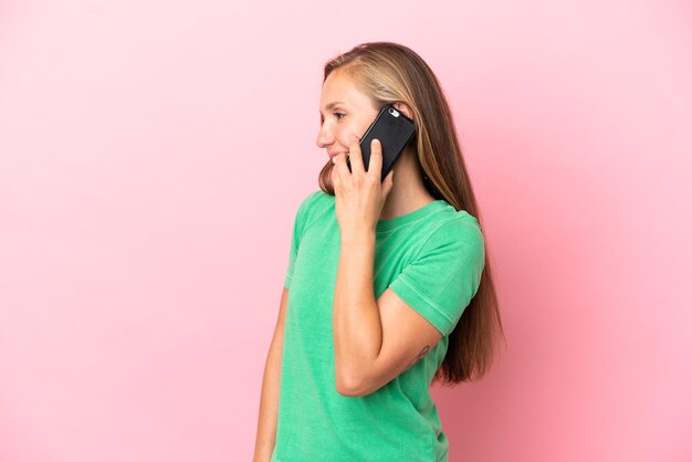 Giovane donna inglese isolata su sfondo rosa che mantiene una conversazione con il telefono cellulare con qualcuno