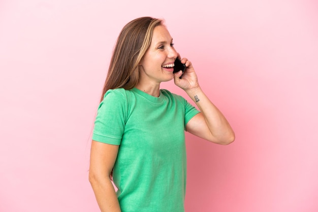 Giovane donna inglese isolata su sfondo rosa che mantiene una conversazione con il telefono cellulare