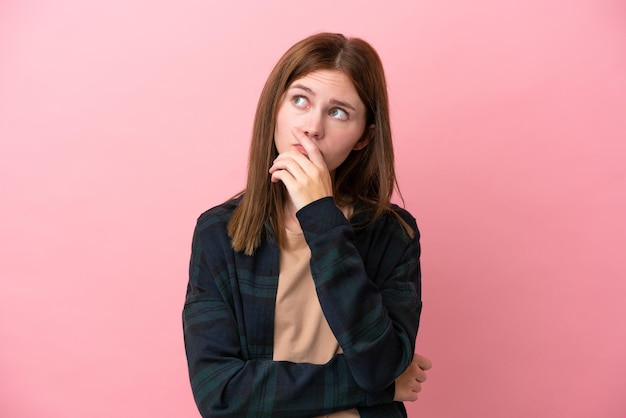 Giovane donna inglese isolata su sfondo rosa con dubbi e con espressione facciale confusa