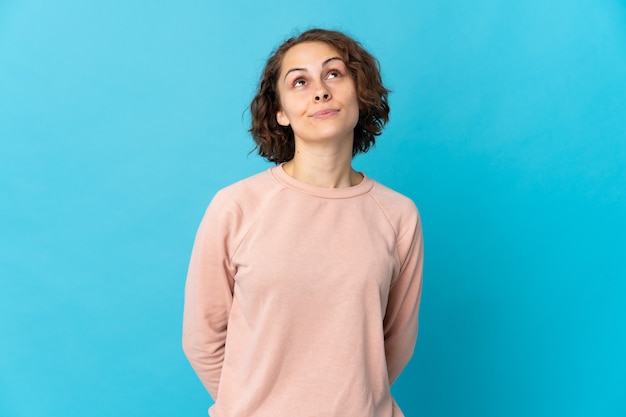 Giovane donna inglese isolata su spazio blu e alzando lo sguardo