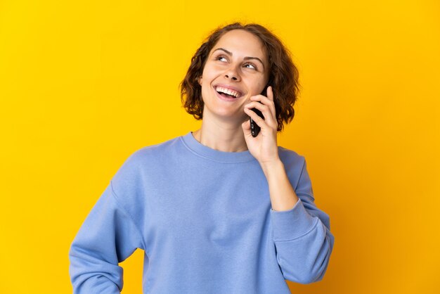 Giovane donna inglese isolata sulla parete gialla mantenendo una conversazione con il telefono cellulare con qualcuno