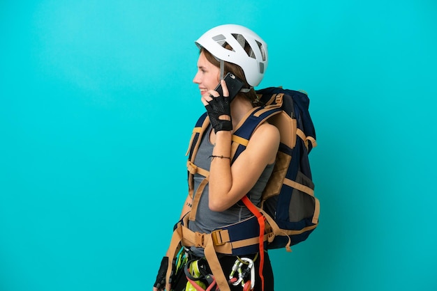 Giovane donna inglese rock climber isolata su sfondo blu che mantiene una conversazione con il telefono cellulare con qualcuno