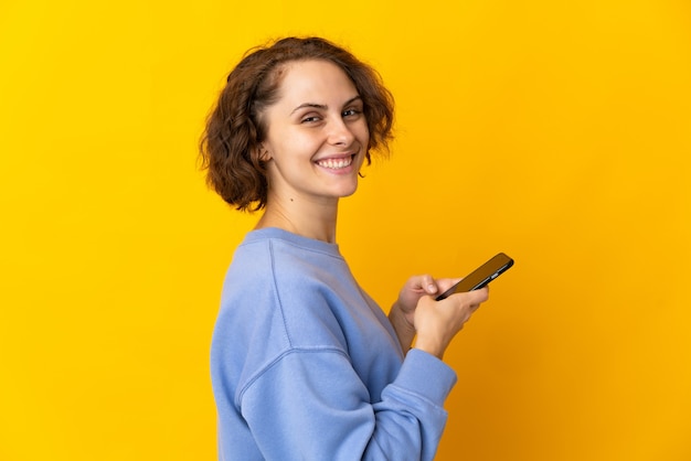 Giovane donna inglese su giallo che invia un messaggio o un'e-mail con il cellulare