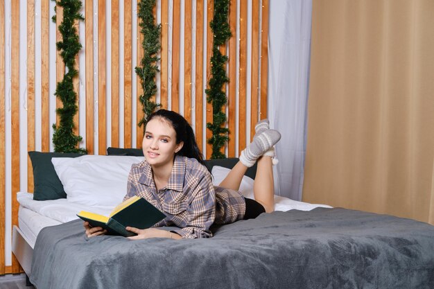 Giovane donna intelligente che legge il libro a letto durante le vacanze