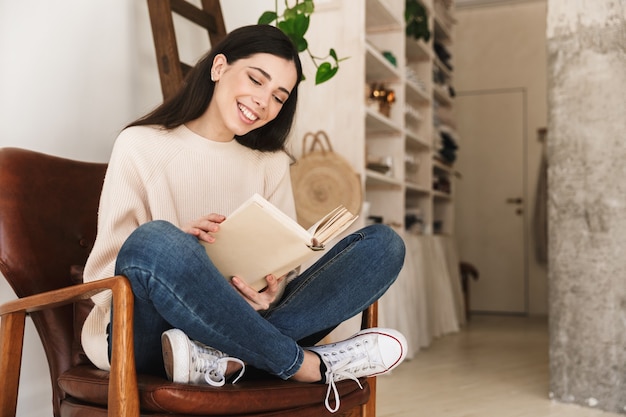 giovane donna intelligente che riposa in appartamento e leggere il libro mentre era seduto sulla sedia