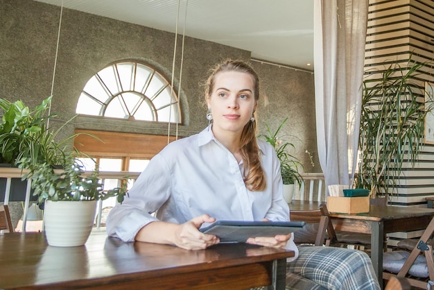 Giovane donna intelligente seduta con gadget portatile e lavoro