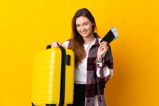 Giovane donna Irlanda isolata sulla parete gialla in vacanza con la valigia e il passaporto