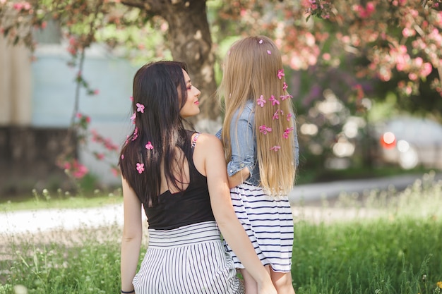 Giovane donna irriconoscibile con la sua piccola figlia in piedi nel parco con fiori tra i capelli. Madre e bambina all'aperto. Famiglia felice.