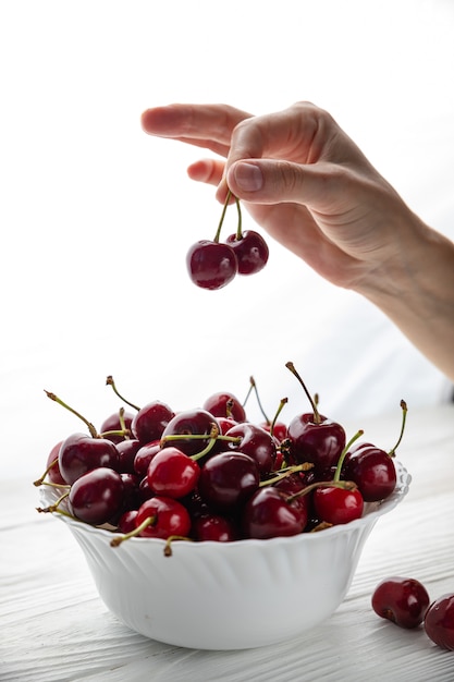 Giovane donna isolata che tiene alcune ciliege in sue mani. Grandi ciliegie rosse su un tavolo bianco