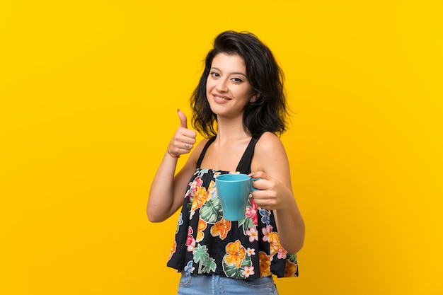 Giovane donna isolata su giallo che tiene tazza di caffè calda