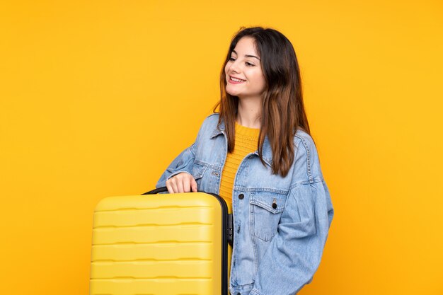 Giovane donna isolata su giallo in vacanza con la valigia di viaggio