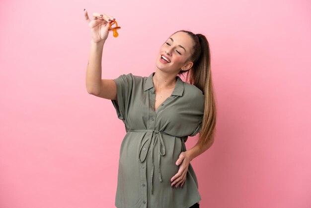 Giovane donna isolata su sfondo rosa incinta e in possesso di un ciuccio