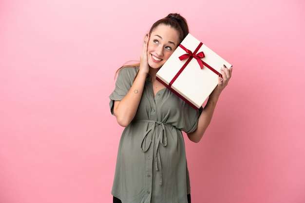 Giovane donna isolata su sfondo rosa incinta e in possesso di un regalo