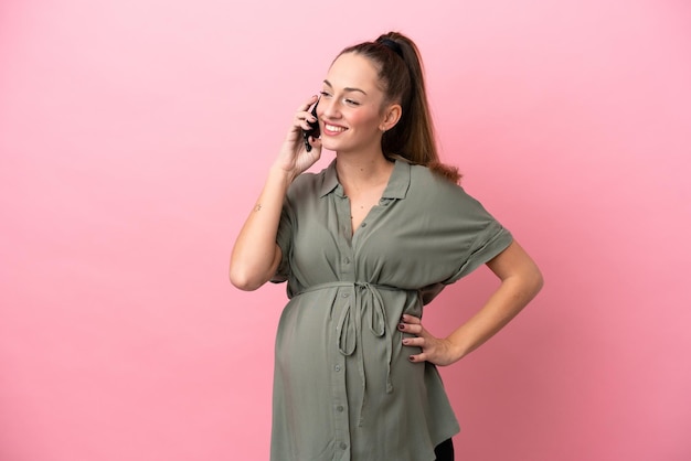 Giovane donna isolata su sfondo rosa incinta e utilizzando il telefono cellulare