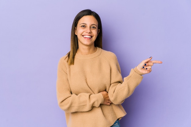 Giovane donna isolata su viola sorridendo allegramente indicando con l'indice di distanza.