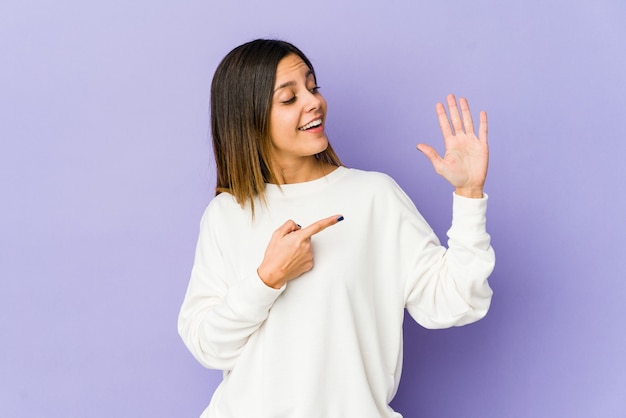 Giovane donna isolata su viola sorridente allegro che mostra il numero cinque con le dita.