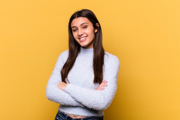 Giovane donna isolata sul muro giallo che si sente sicura di sé, incrociando le braccia con determinazione.