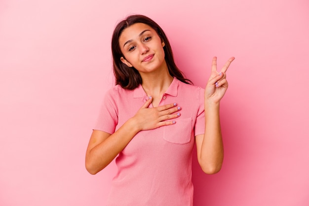 Giovane donna isolata sul muro rosa prestando giuramento, mettendo la mano sul petto