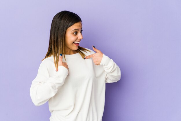 Giovane donna isolata sul muro viola sorpreso indicando con il dito, sorridendo ampiamente.