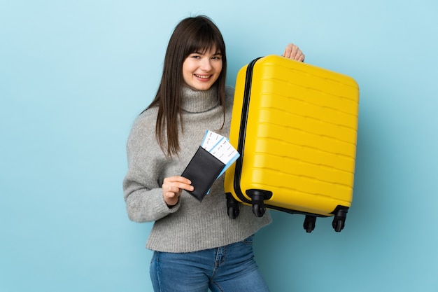 Giovane donna isolata sull'azzurro in vacanza con la valigia e il passaporto