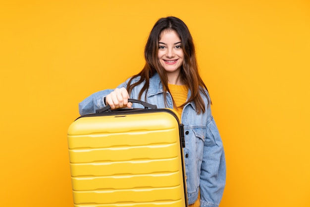 Giovane donna isolata sulla parete gialla in vacanza con la valigia di viaggio e infelice