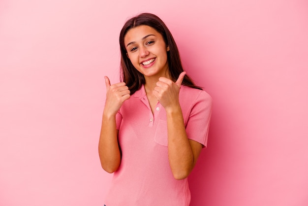 Giovane donna isolata sulla parete rosa che alza entrambi i pollici in su, sorridente e sicura