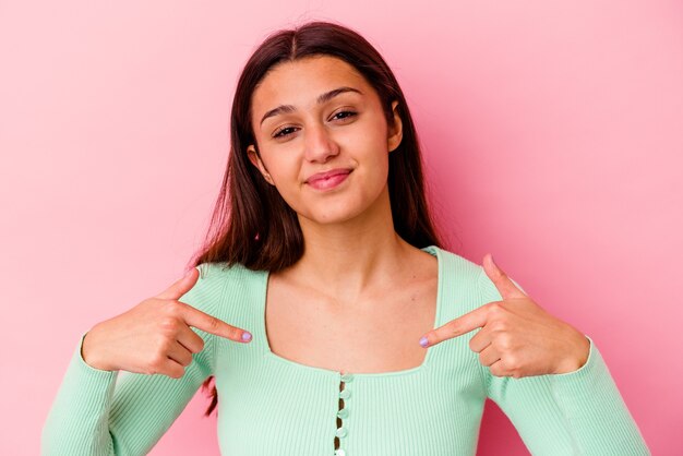 Giovane donna isolata sulla persona del muro rosa che indica a mano uno spazio della copia della maglietta, orgoglioso e fiducioso