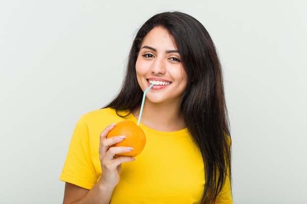 Giovane donna ispanica che beve un succo d'arancia con una cannuccia
