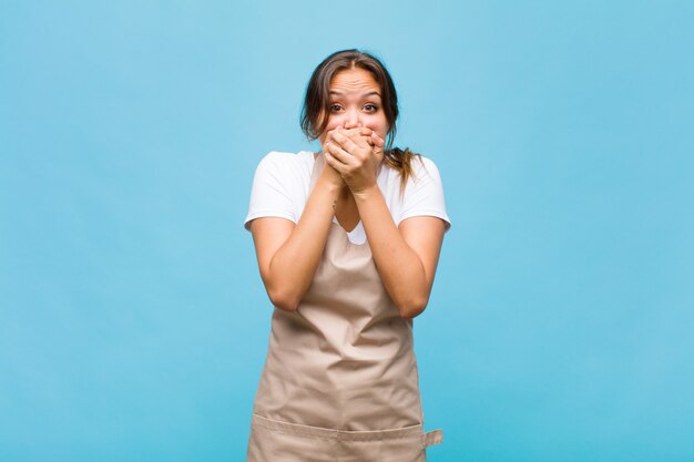 Giovane donna ispanica che copre la bocca con le mani con un'espressione scioccata e sorpresa, mantenendo un segreto o dicendo oops