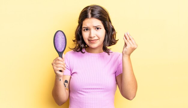 Giovane donna ispanica che fa un gesto capice o denaro, dicendoti di pagare. concetto di spazzola per capelli