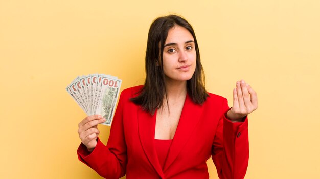 Giovane donna ispanica che fa un gesto di capice o denaro che ti dice di pagare il concetto di banconote in dollari