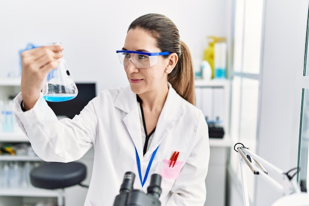 Giovane donna ispanica che indossa l'uniforme dello scienziato che tiene la provetta in laboratorio