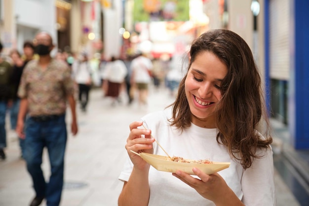 Giovane donna ispanica che mangia takoyaki in via Dotonbori a Osaka in Giappone
