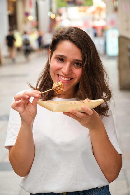 Giovane donna ispanica che mangia takoyaki nella strada Dotonbori a Osaka, in Giappone