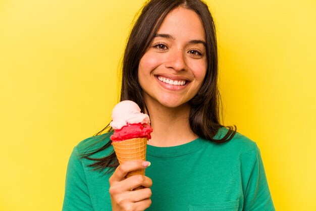 Giovane donna ispanica che mangia un gelato isolato su sfondo giallo